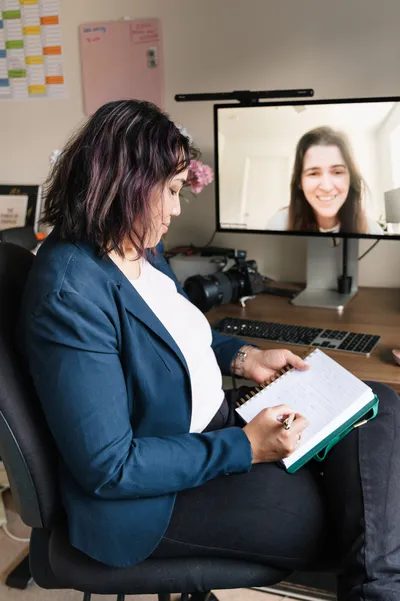 Pet photography business coach Ina J taking notes during a coaching call, a client visible on the monitor